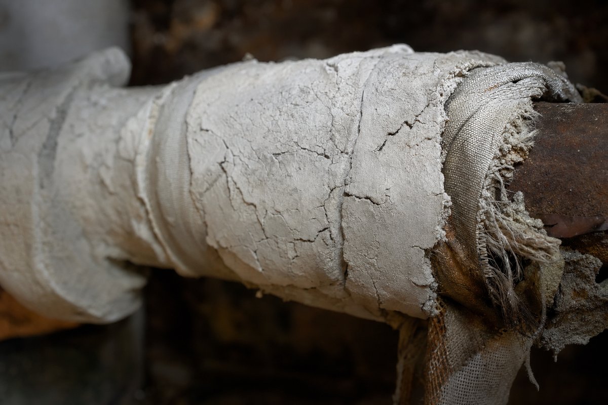 Calorifugeage d'époque sur des conduites de chauffage en cave : le matériau à faire vérifier avant toute dépose.