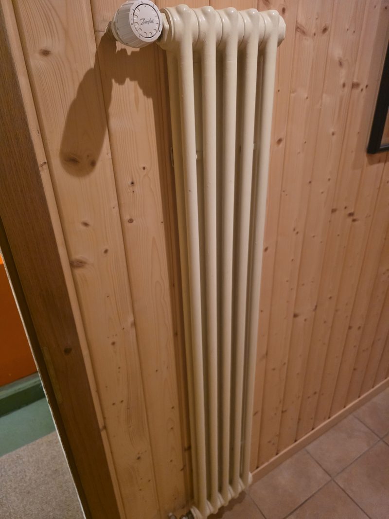 Radiateur à colonnes avec tête thermostatique sur un mur en lambris